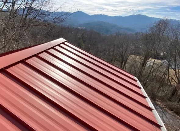 Red standing seam metal roof installed on a mountain home near Asheville with Blue Ridge Mountains in the background.