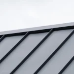Standing seam metal roof ridge with a grey sky behind.