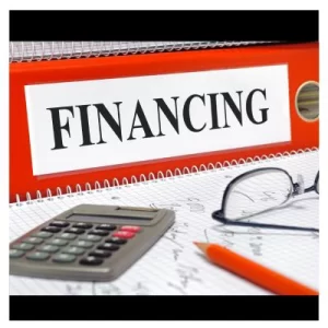 Red binder labeled with financing on a table with a calculator, pencil, and a pair of glasses with figures written on a piece of paper.