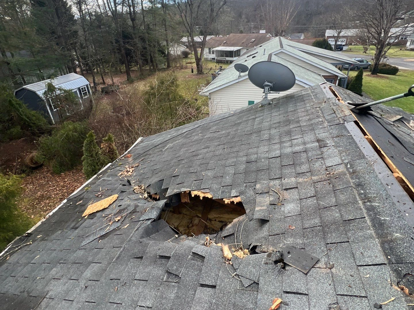 Storm-damaged residential roof with a large hole and broken shingles—Quantum Roofing provides 24/7 emergency roof repair to restore safety and prevent further damage.