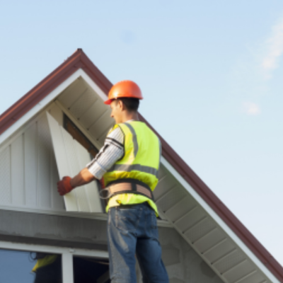 A technician conducting a residential roof inspection, wearing safety gear while examining the eaves of a home.